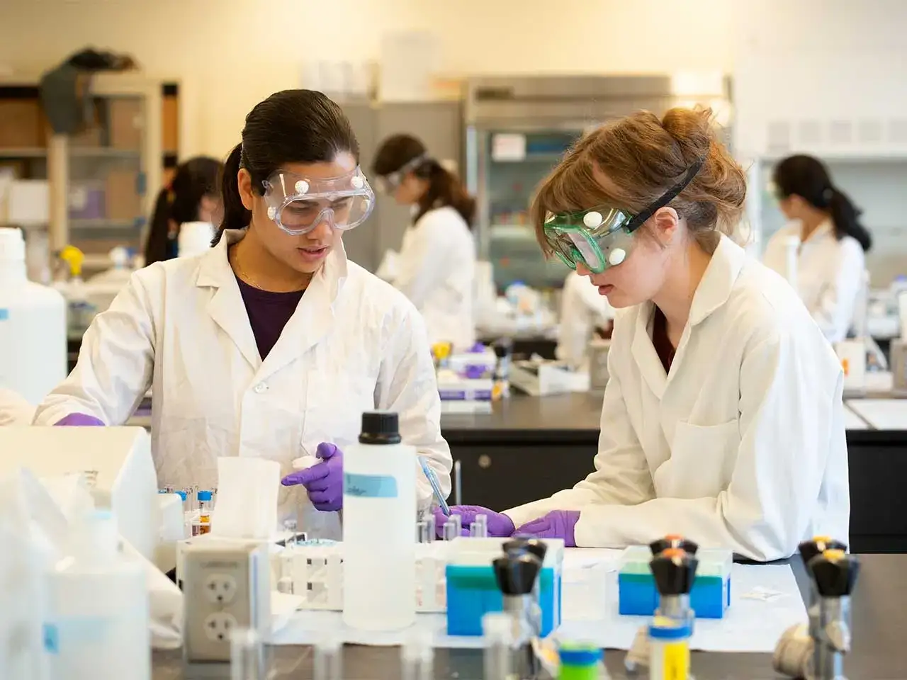 Zwei Studentinnen im Labor, die sich auf ihr lebensmittelchemie studium konzentrieren. Sie tragen Laborkittel und Schutzbrillen.