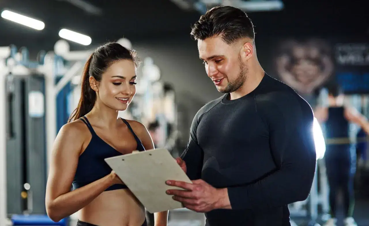 Ein Trainer und eine Kundin besprechen Trainingspläne. Das Gehalt eines Sport- und Fitnesskaufmanns nach der Ausbildung ist attraktiv.