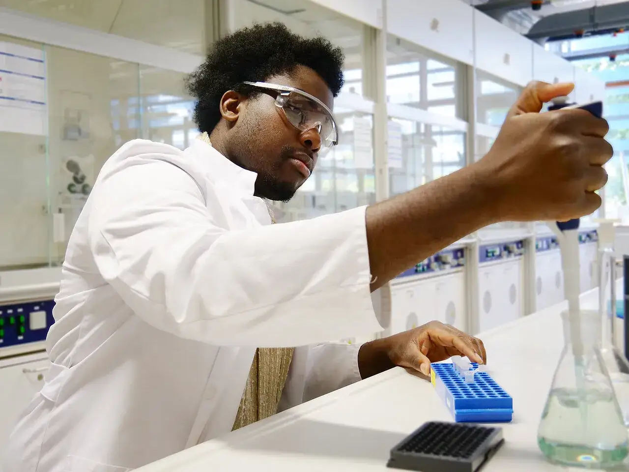 Ein Mann mit Schutzbrille und Laborkittel arbeitet konzentriert mit einer Pipette und Röhrchen. Sein diplom studium in Chemie ist hier in vollem Gange.