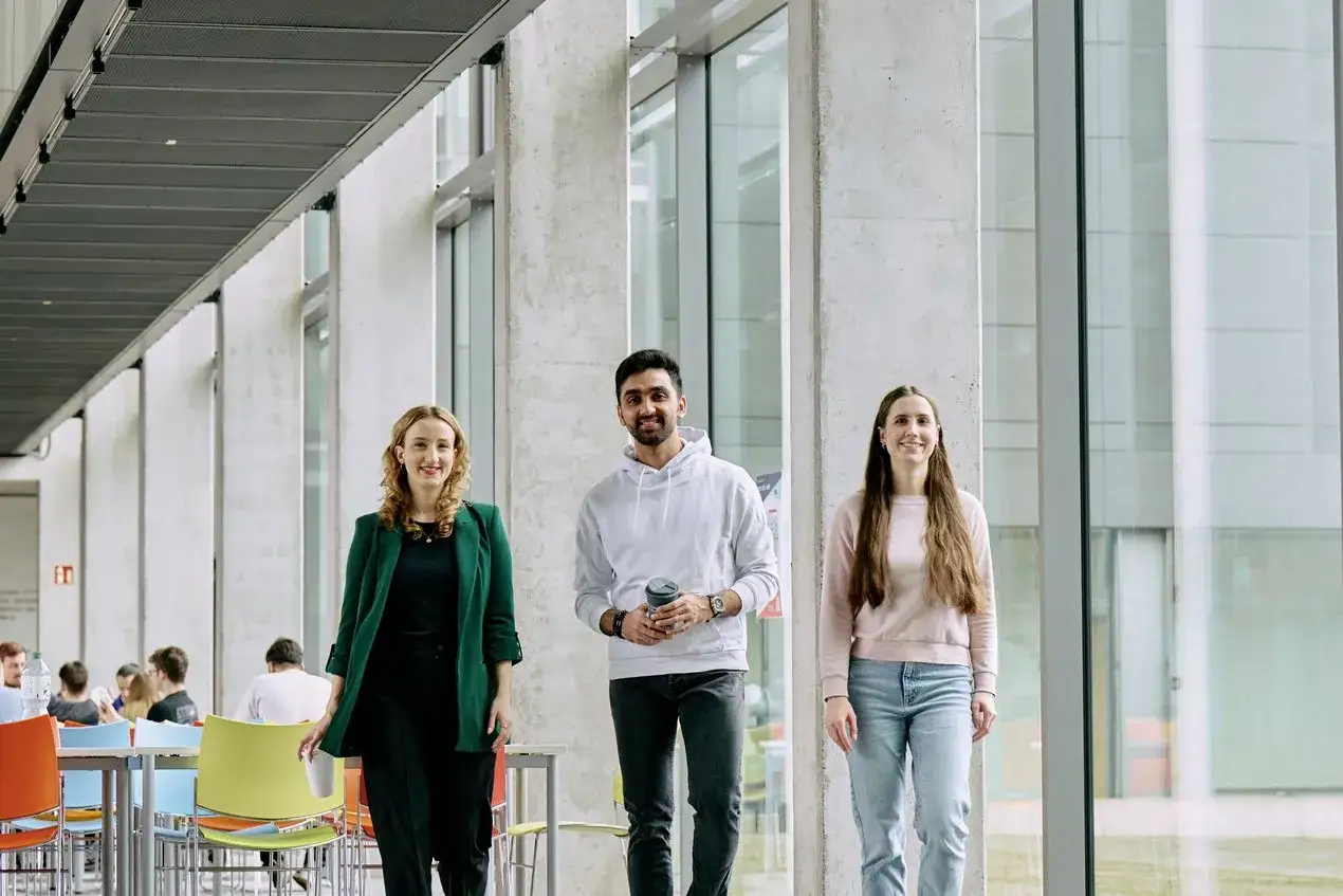 Drei Studierende, die einen Bachelor in Betriebswirtschaft anstreben, gehen lächelnd durch einen modernen Campus-Flur.