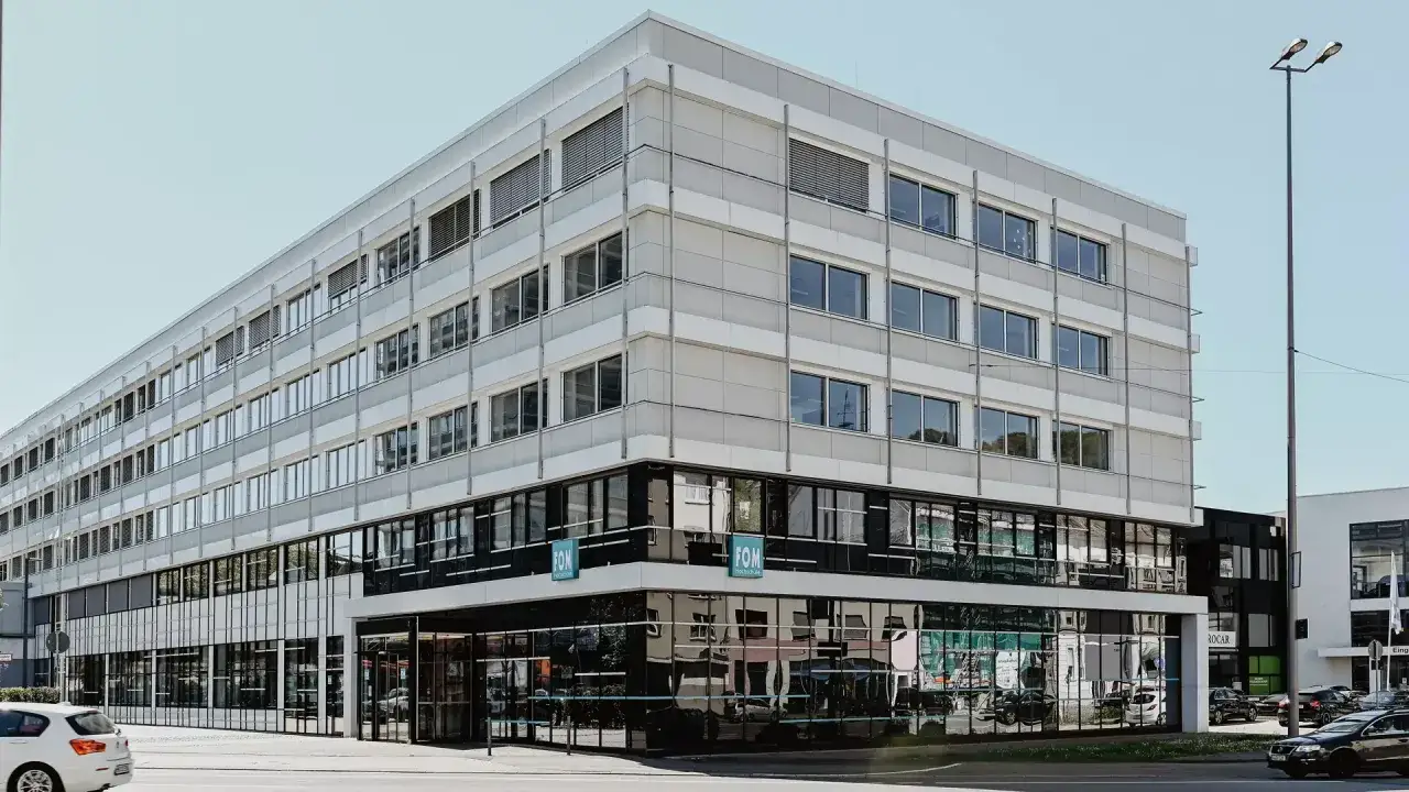 Modernes Gebäude der FOM Hochschule in Wuppertal. Helle Fassade mit vielen Fenstern, unten dunkle Glasfront.