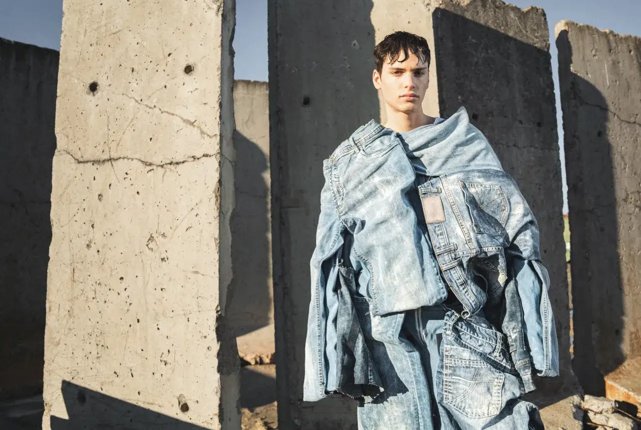 Junger Mann in einem surrealen Outfit aus Jeans, inspiriert vom textildesign studium. Betonruinen im Hintergrund.