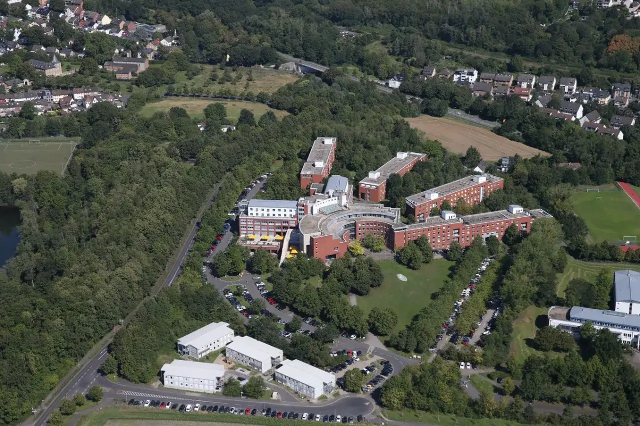 Luftaufnahme des Campus der HS BUND mit mehreren Gebäuden, Parkplätzen und viel Grün.