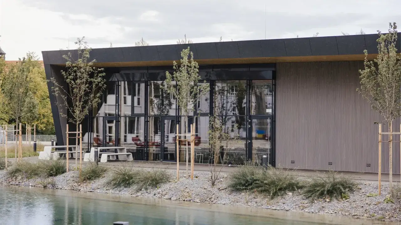 Moderne Architektur am Campus der Landshut University of Applied Sciences. Ein Teich spiegelt das Gebäude mit Glasfassade und Holzverkleidung.