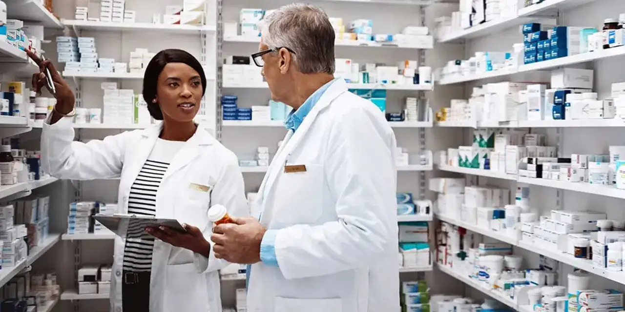 Zwei Apotheker im Gespräch vor Regalen voller Medikamente. Sie arbeiten an ihrem Traumberuf, helfen Menschen mit ihren Gesundheitsproblemen.