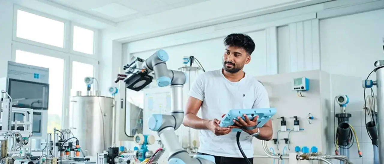 Ein junger Mann, der ein Bachelor-Studium absolviert, ist ein Ingenieur, der einen Roboterarm in einem Labor steuert.