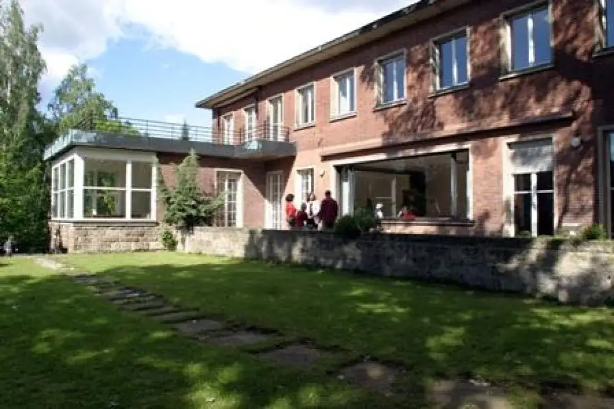 Ein Gebäude der Touro University Berlin mit Garten und Terrasse. Menschen stehen auf der Terrasse.