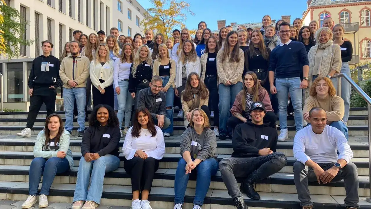 Gruppe von Studierenden der HS Fresenius Hamburg posiert lächelnd auf einer Treppe.