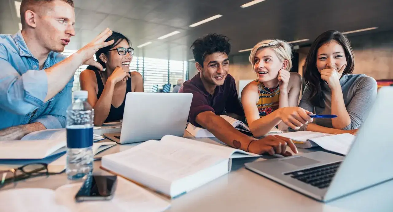 Fünf Studierende diskutieren angeregt über ihren Bachelor of Arts BWL. Sie arbeiten zusammen an Laptops und Büchern.