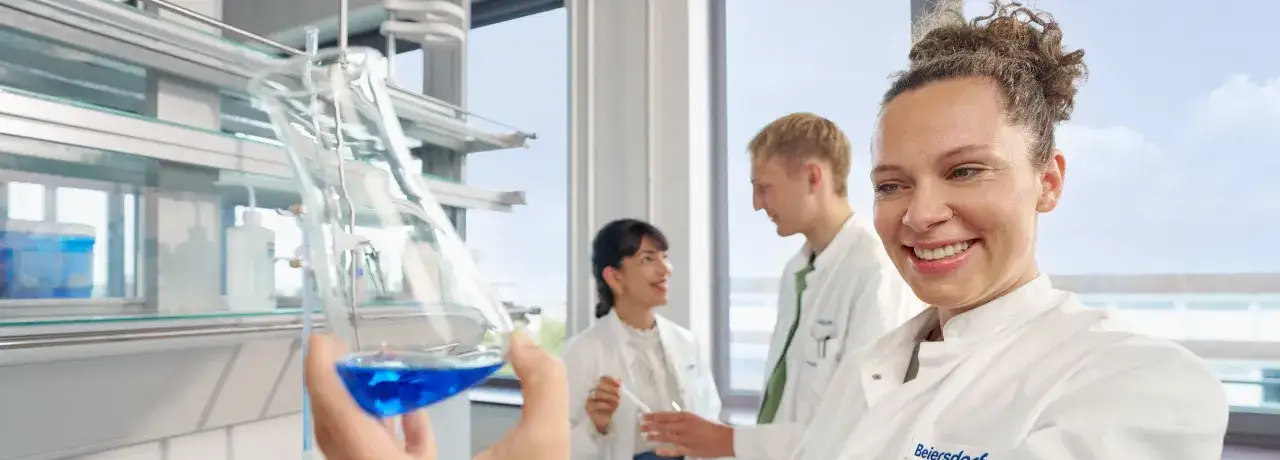Ein Promotionsstudium in der Forschung: Drei Wissenschaftler im Labor, eine hält einen Kolben mit blauer Flüssigkeit.